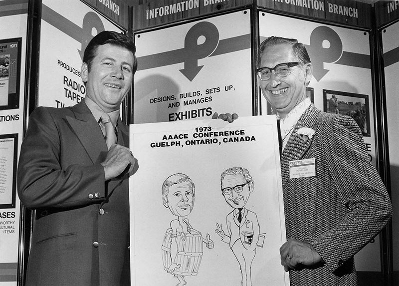 Two former ACE members hold a poster for the 1973 AAACE Conference in Ontario, Canada.